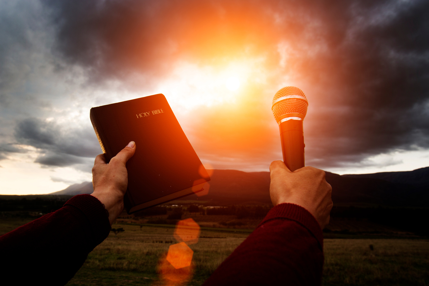 Hand holds bible and microphone up towards gray clounds